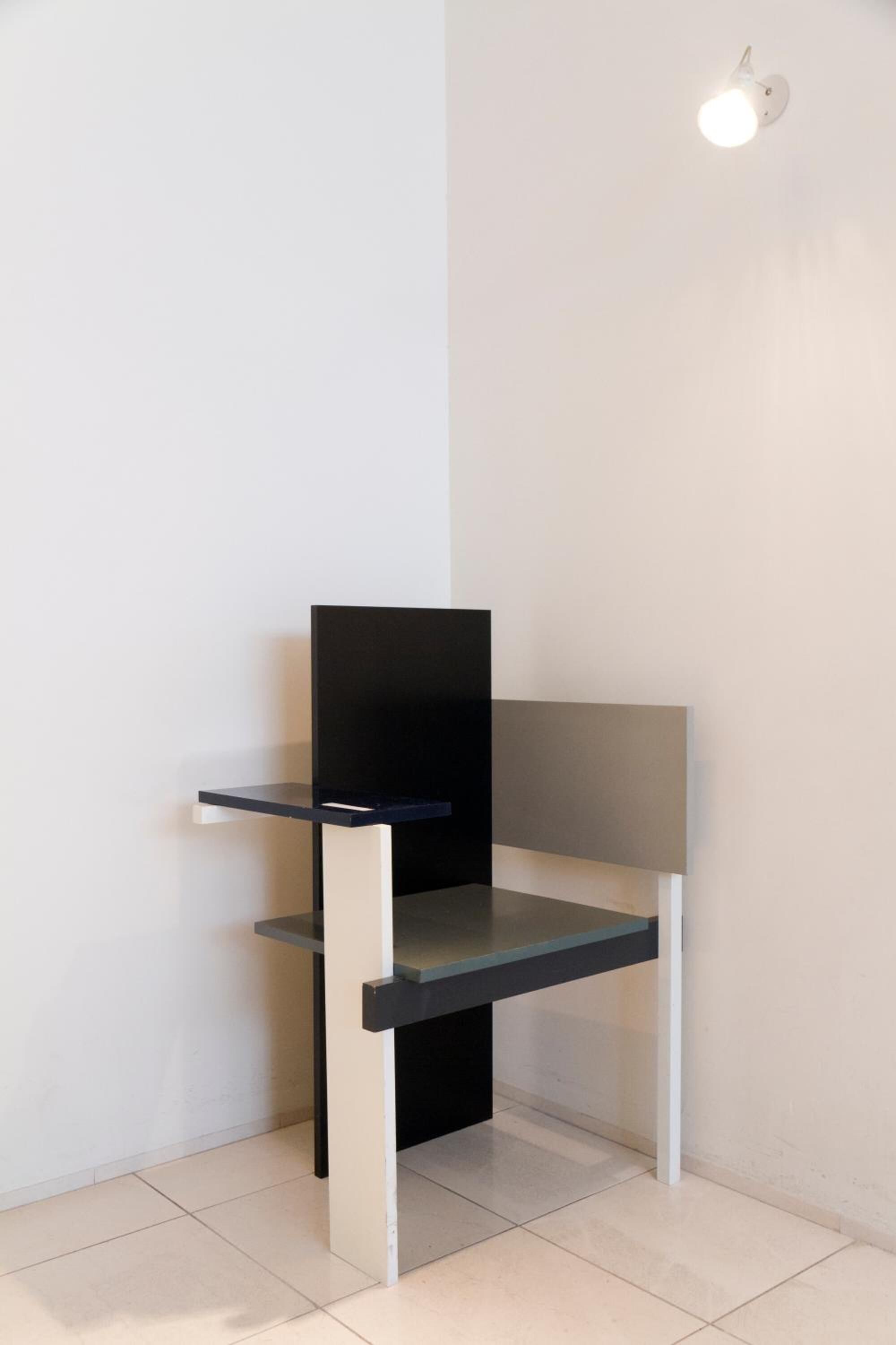 A corner of a room with a white wall, a black and white desk, and a white floor.