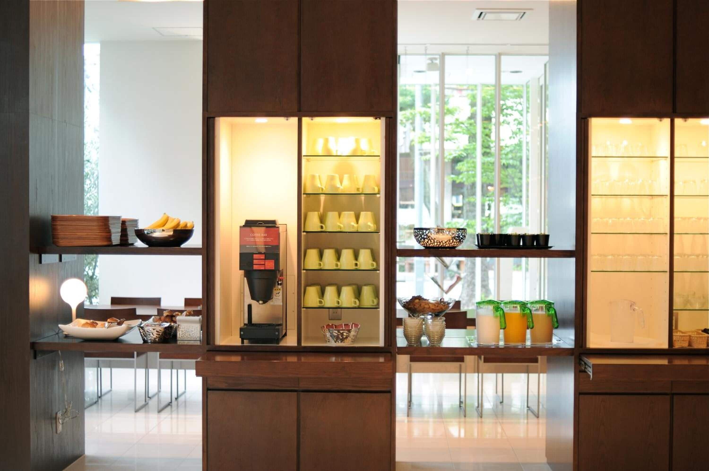A modern cafe with a coffee machine, shelves of cups, and a window view.