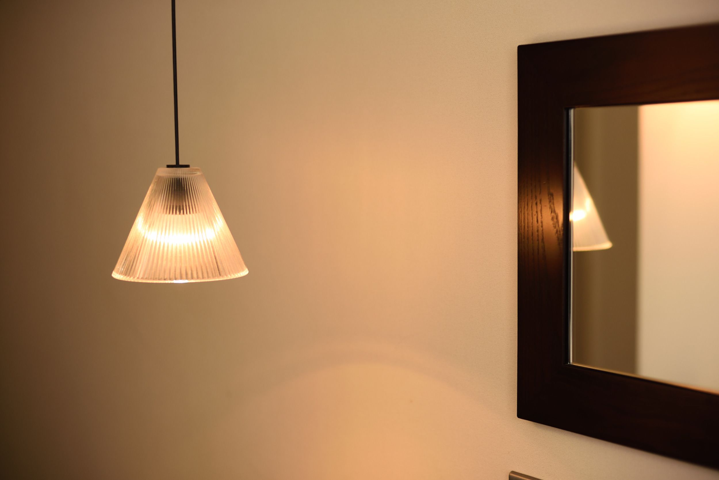 A pendant light fixture with a ribbed design hanging from the ceiling, a wall-mounted mirror, and a portion of a dark-framed picture frame.