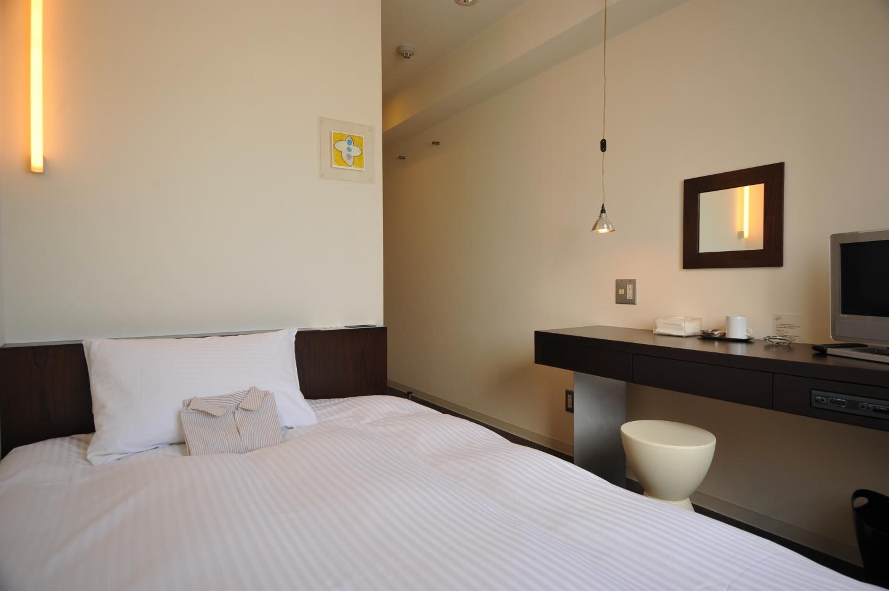 Een hotelkamer met een bed, een bureau, een stoel, een televisietoestel en een spiegel.