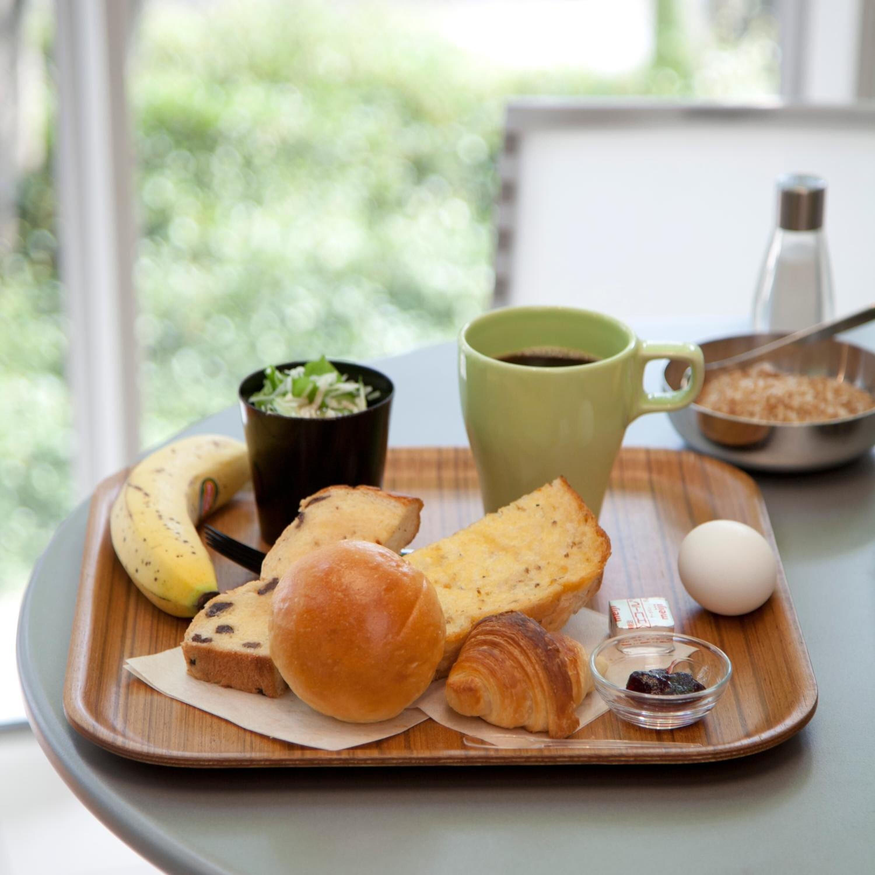 Una bandeja con cruasanes, un plátano, un cuenco pequeño de bayas, una taza verde y una rebanada de pan.