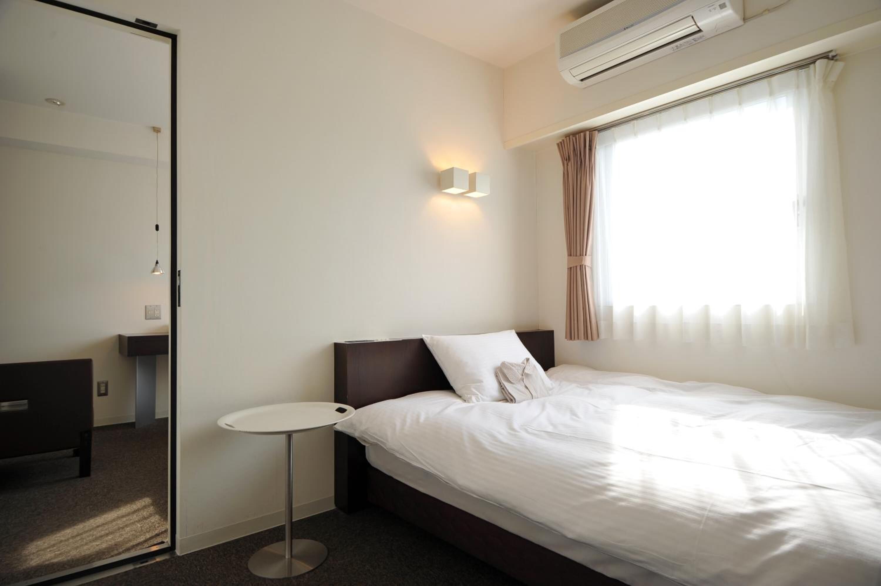A hotel room with a bed, bedside table, and a window with curtains.