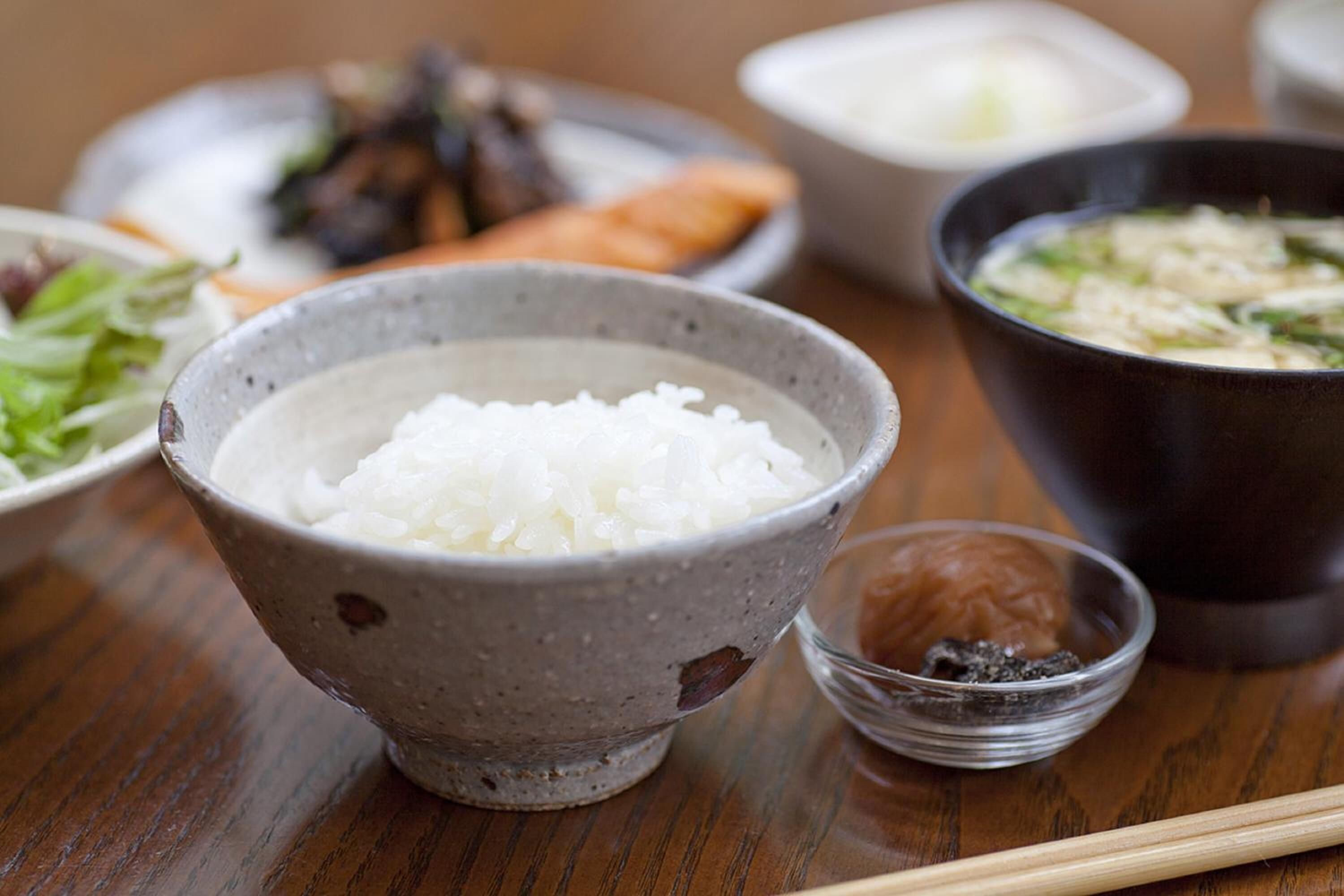 A table with a bowl of white rice, a small bowl of sauce, and a bowl of soup.