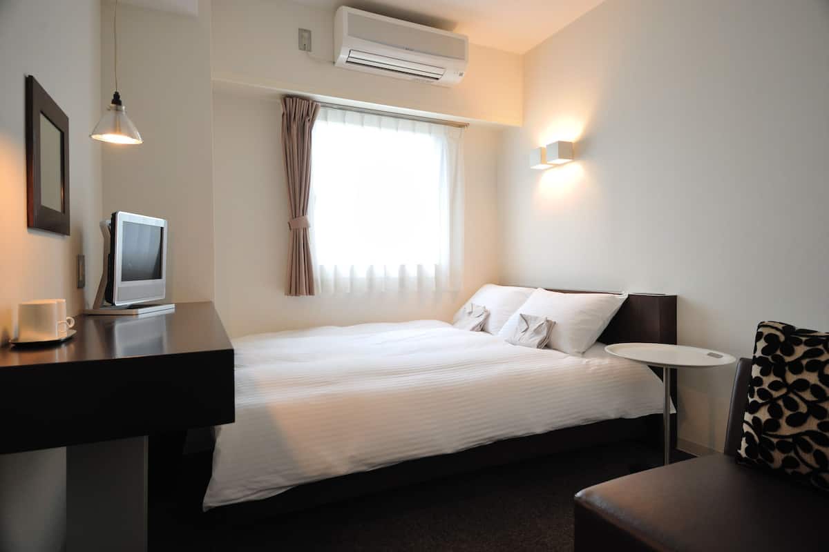 A hotel room with a bed, a desk with a computer, a small table, and a chair.