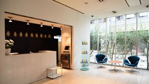 A modern reception area with a reception desk, a self-service kiosk, and seating with a view of the outdoors. - 7 Days Hotel Plus (Kochi)