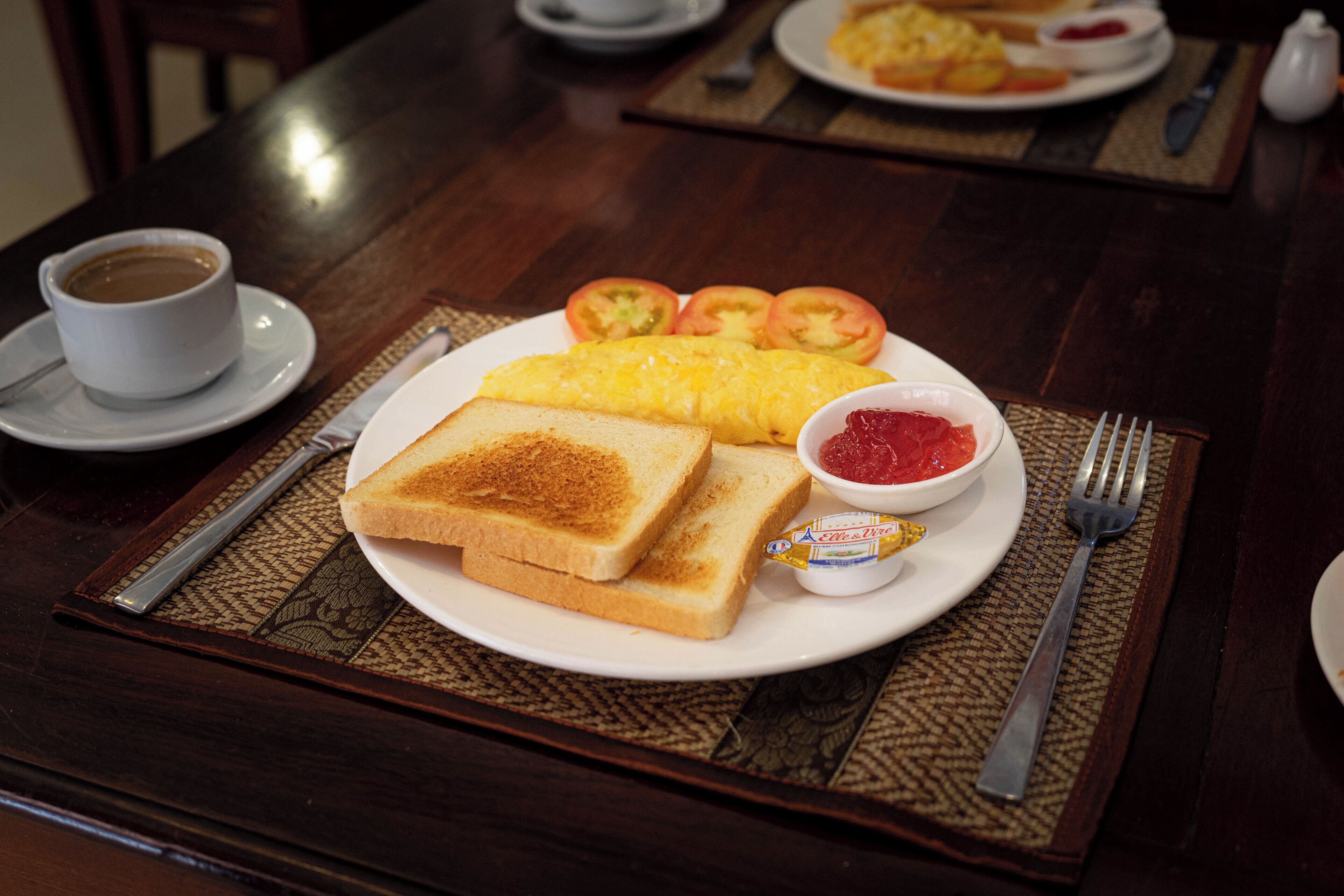 Een ontbijt bord met toast, eieren, tomaten en jam op een tafel.