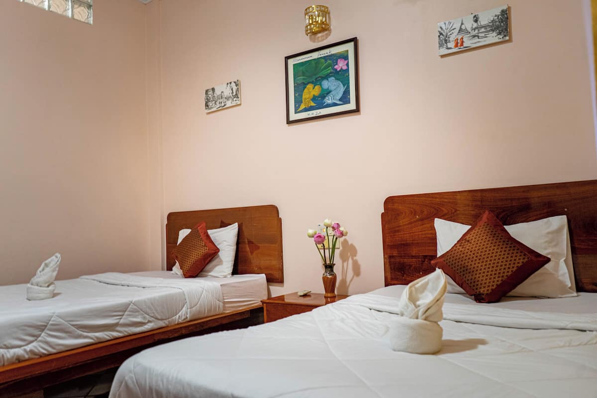 Une chambre d’hôtel avec deux lits, des têtes de lit en bois, du linge de lit blanc, une petite table avec un vase de fleurs et des œuvres d’art murales.