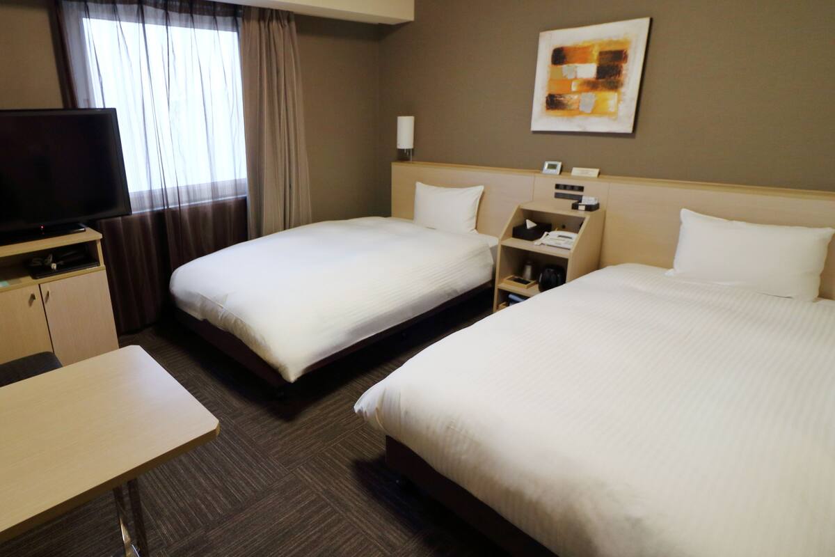 A hotel room with two beds, a TV, a desk, and a painting on the wall.