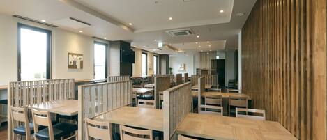 A modern dining area with wooden tables and chairs, partitioned booths, and recessed ceiling lighting.