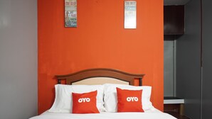 A bed with white bedding and two red pillows with "OYO" text, a wooden headboard, and a bright orange wall with two signs above the bed. - OYO 89646 Panvill Resort (Pangkor Island)