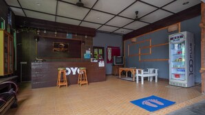 A PanVilla Resort reception area with a wooden counter, two stools, a television, a refrigerator, and a blue mat on the floor. - OYO 89646 Panvill Resort (Pangkor Island)