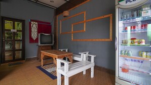 A room with a 100 PLUS refrigerator stocked with beverages, a wooden table with benches, a television on a stand, and a 'STAFF ONLY' door. - OYO 89646 Panvill Resort (Pangkor Island)