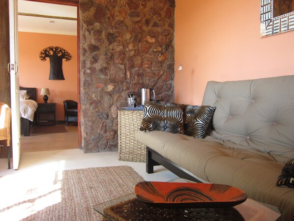 Uma sala de estar com parede de pedra, um sofá com almofadas estampadas, uma mesa de centro e uma mesinha de vime com uma chaleira e xícaras.