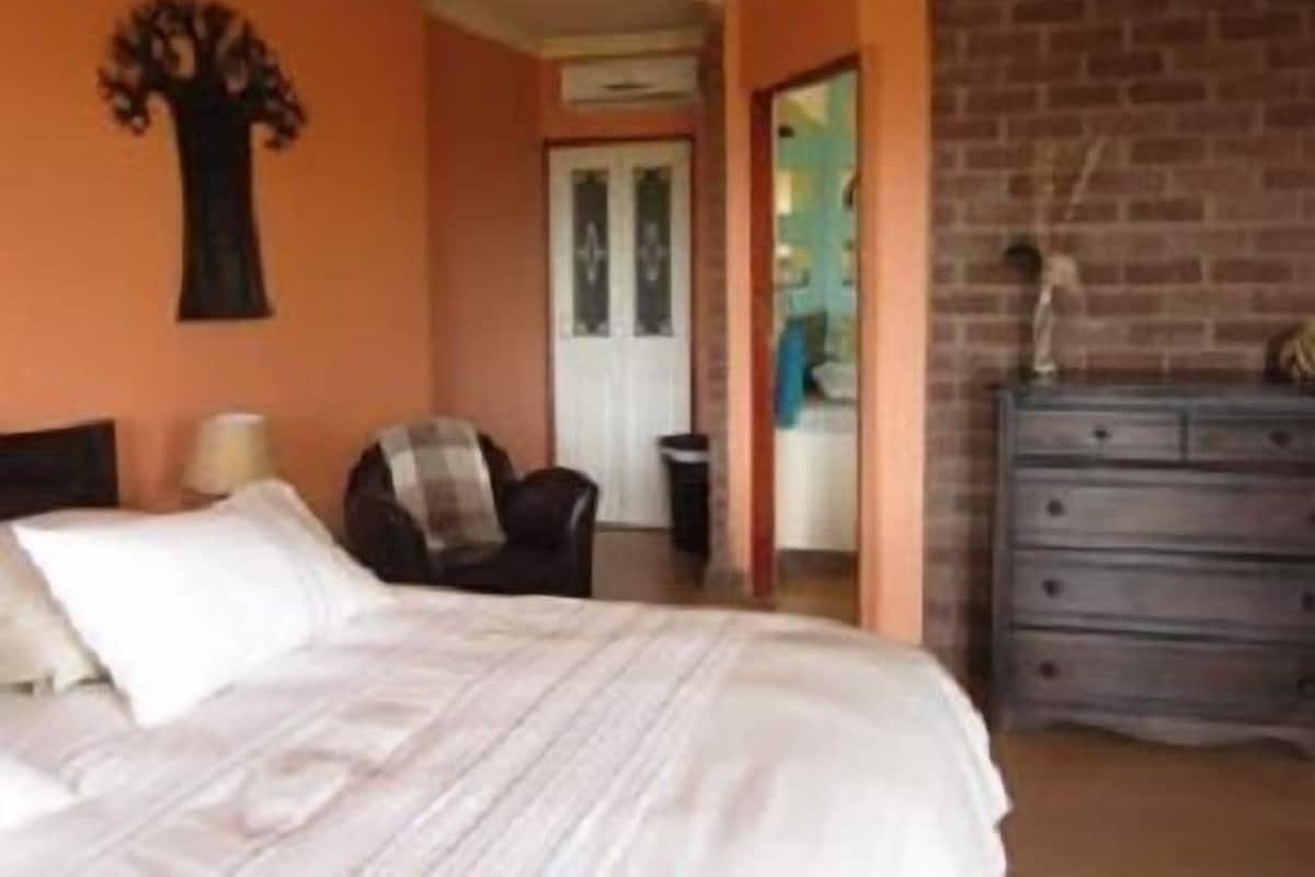 A bedroom with a bed, a chair, a dresser, and a wall decoration.
