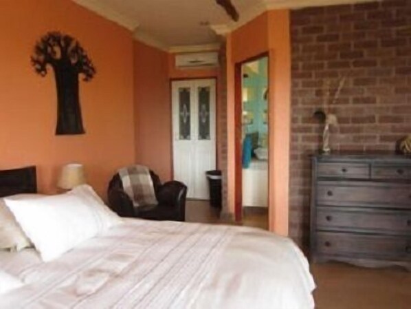 A bedroom with a bed, a chair, a dresser, and a wall decoration. - Marula Cottage (Thabazimbi)