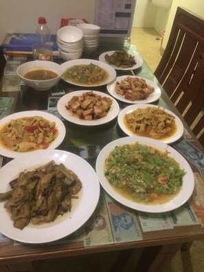 A dining table with multiple plates of food, a bottle, and some bowls. - River Park Homestay and Hostel (Da Nang)