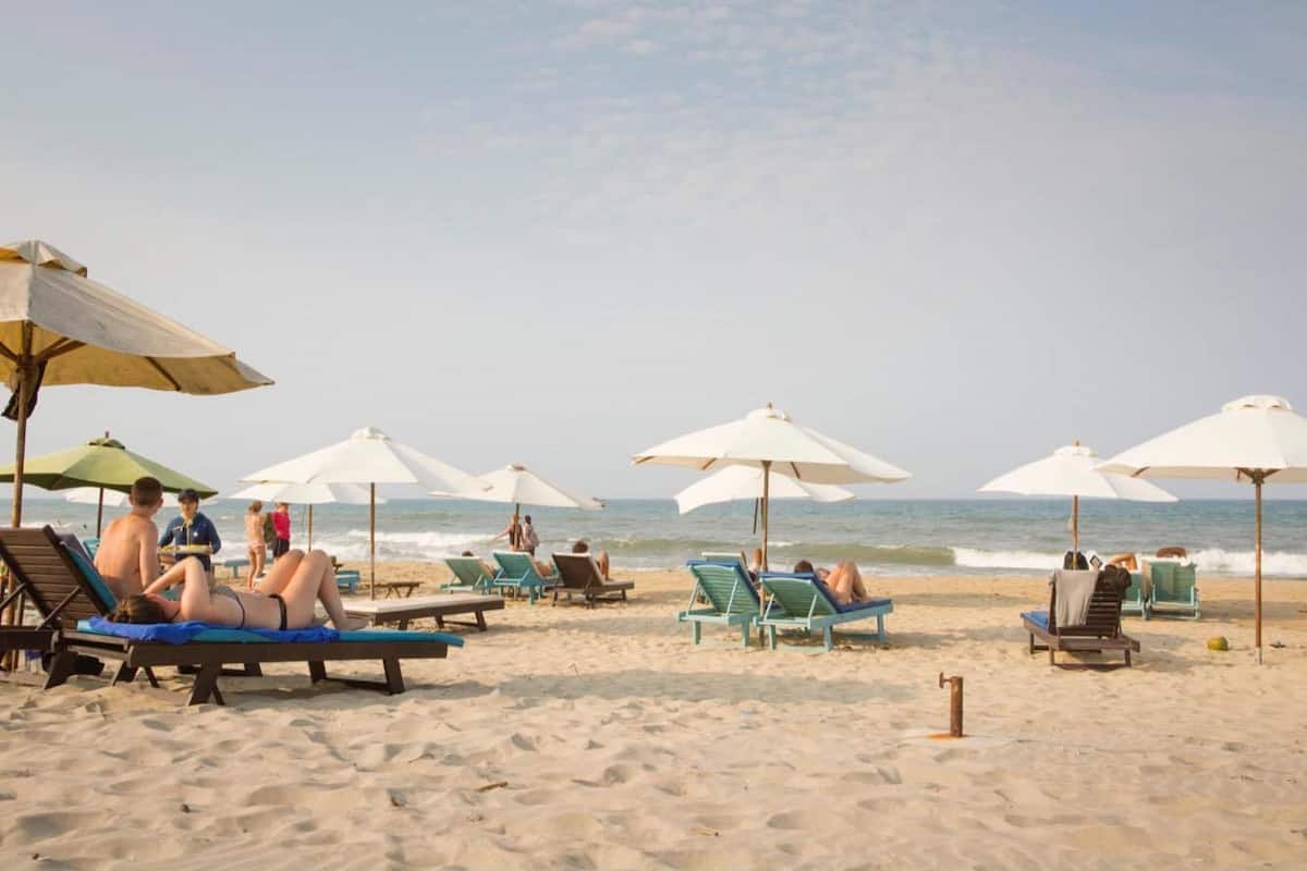 Ein Strand mit Liegestühlen und Sonnenschirmen, ein sandiger Uferstreifen und das Meer im Hintergrund.