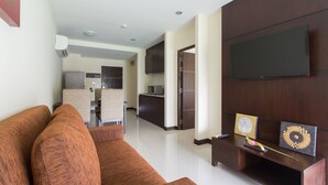 A modern living room with a brown sofa, a flat-screen TV mounted on the wall, and a small table with decorative items. - The Lai Thai Luxury Condominiums (Krabi)
