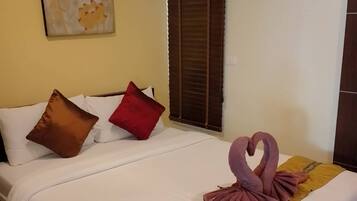 Una habitación de hotel con cama, almohadas, una manta, una toalla con forma de cisne, un cuadro y una ventana con persianas.