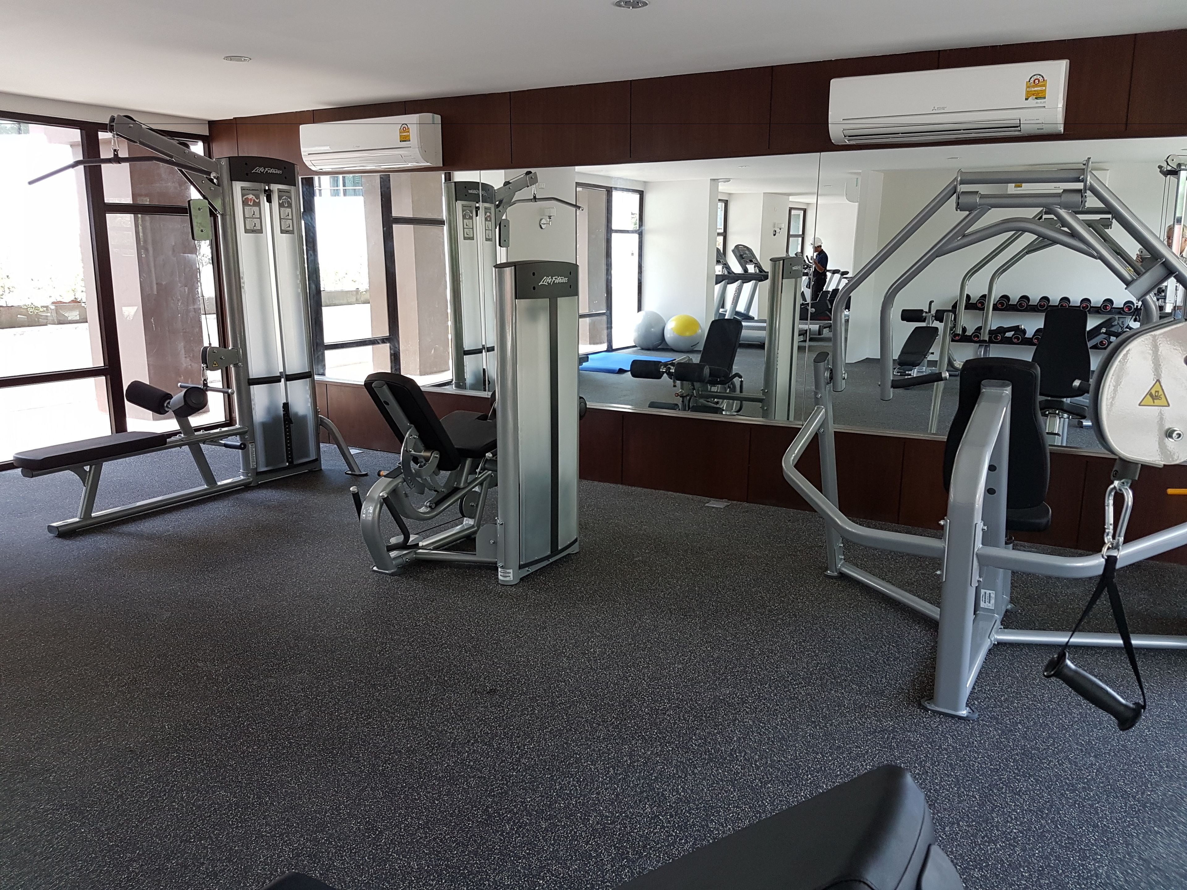 A gym with various exercise equipment, large windows, and an air conditioning unit.