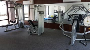 A gym with various exercise equipment, large windows, and an air conditioning unit.