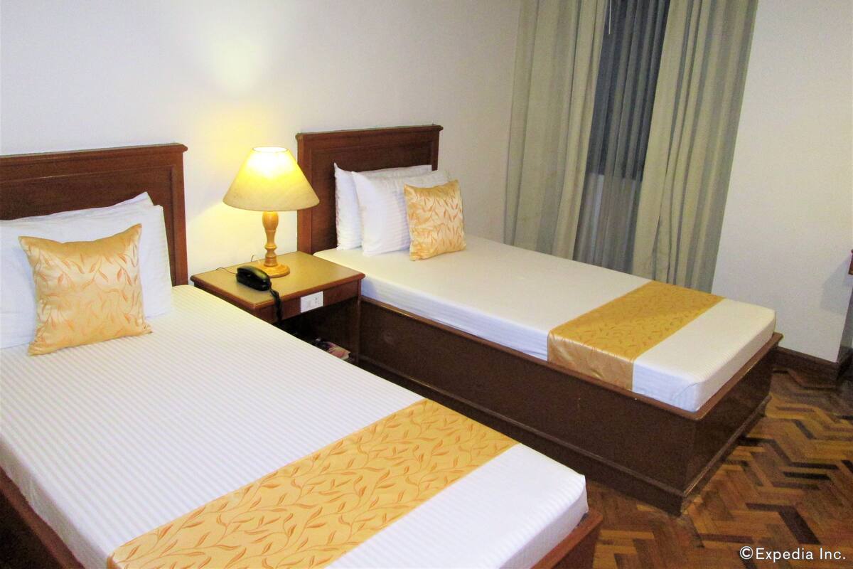 A hotel room with two beds, a bedside table with a lamp, and a telephone.