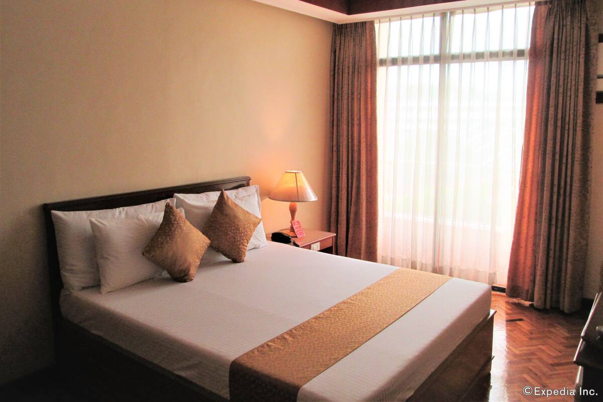 A hotel room with a large bed, a bedside lamp, and a window with curtains.