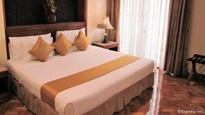 A hotel room with a large bed, a wooden headboard, a nightstand with a lamp, and a window with curtains. - Maxandrea Hotel (Cagayan de Oro)