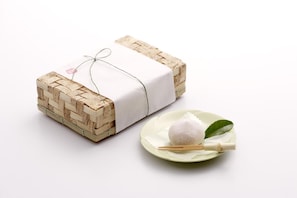 A gift wrapped in a woven basket with a white cloth and tied with a string.
