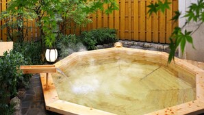 A traditional wooden hot spring bath surrounded by stone tiles and lush greenery. - Tsukagoshiyashichibee (Shibukawa)