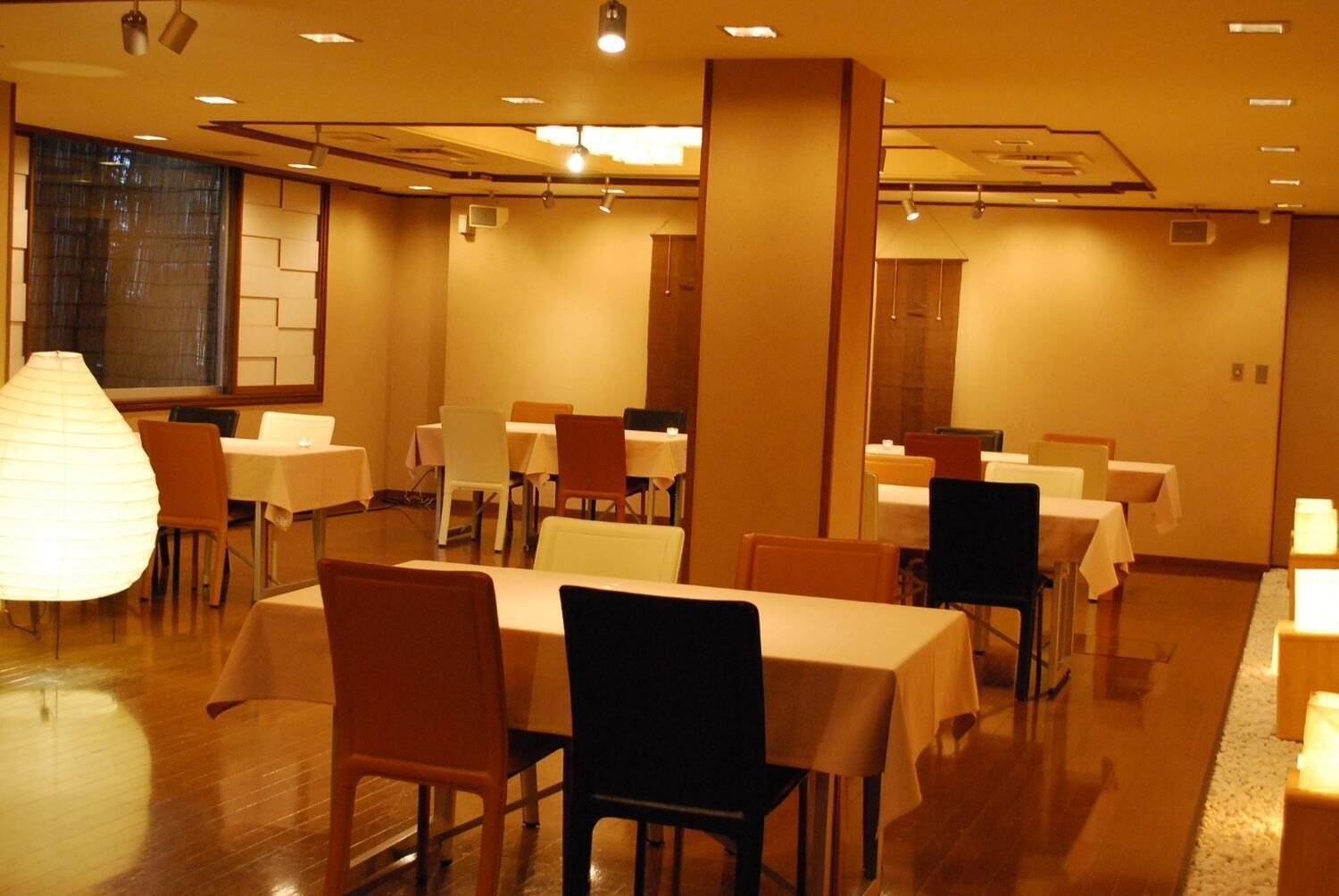 A hotel dining area with multiple tables and chairs, a large decorative lamp, and a modern interior design.