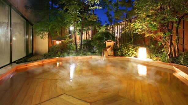 A wooden hot tub surrounded by lush greenery and wooden fences, with a small wooden structure in the background. - Tsukagoshiyashichibee (Shibukawa)