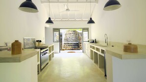 A modern kitchen with white cabinetry, a central island, and pendant lighting. A stone staircase leads to an outdoor area.