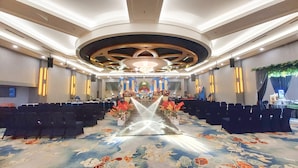 Een ruime zaal met rijen stoelen, een podium met bloemdecoratie en een kroonluchter.