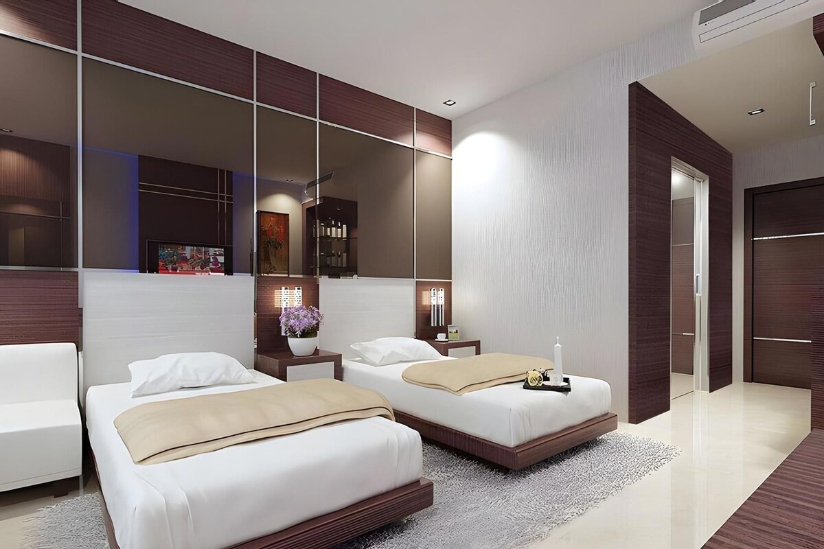 A modern hotel room with two beds, a large mirror, and a nightstand with a lamp.