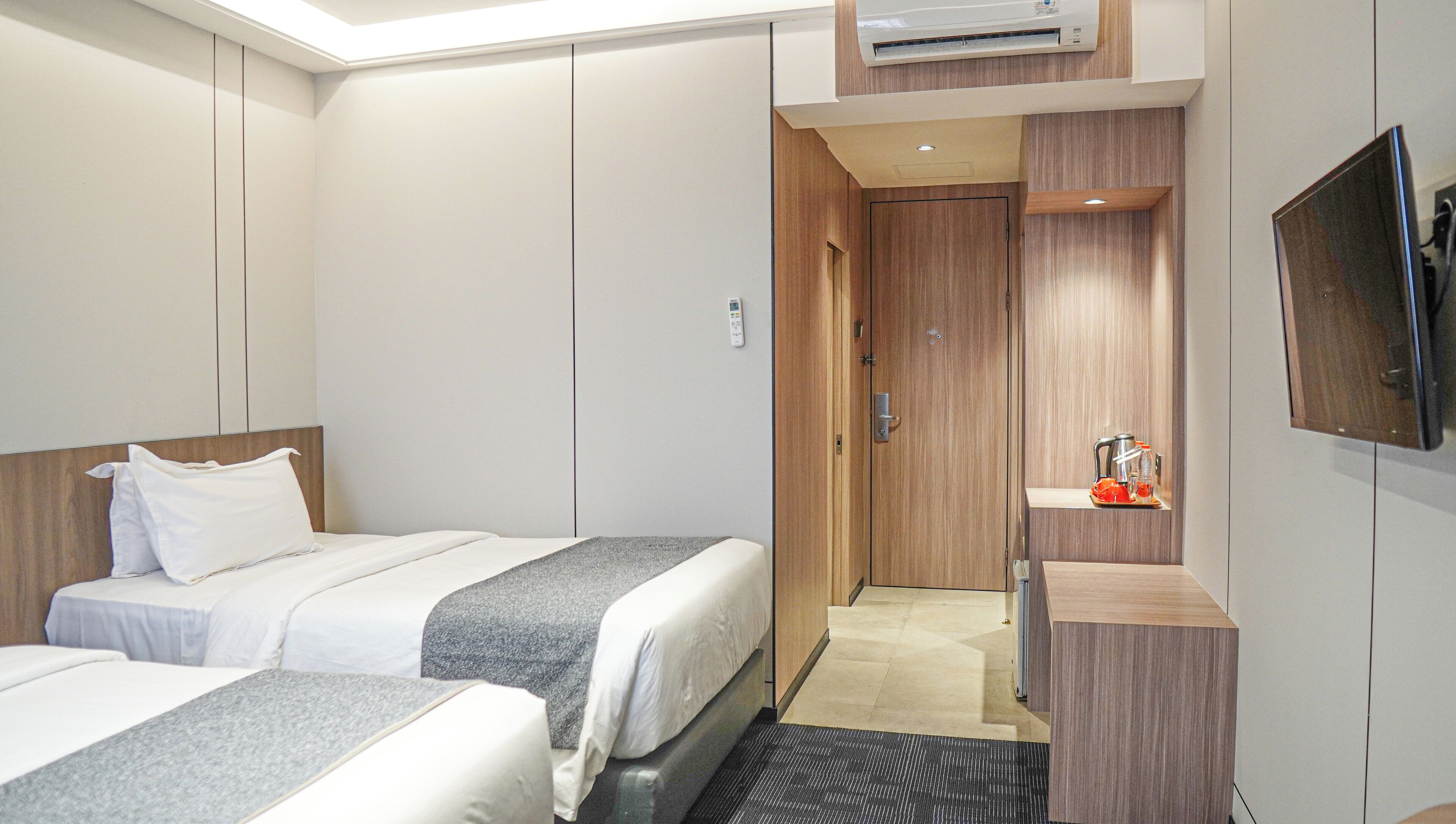 A hotel room with two beds, a TV, a coffee maker, and a wooden wardrobe.