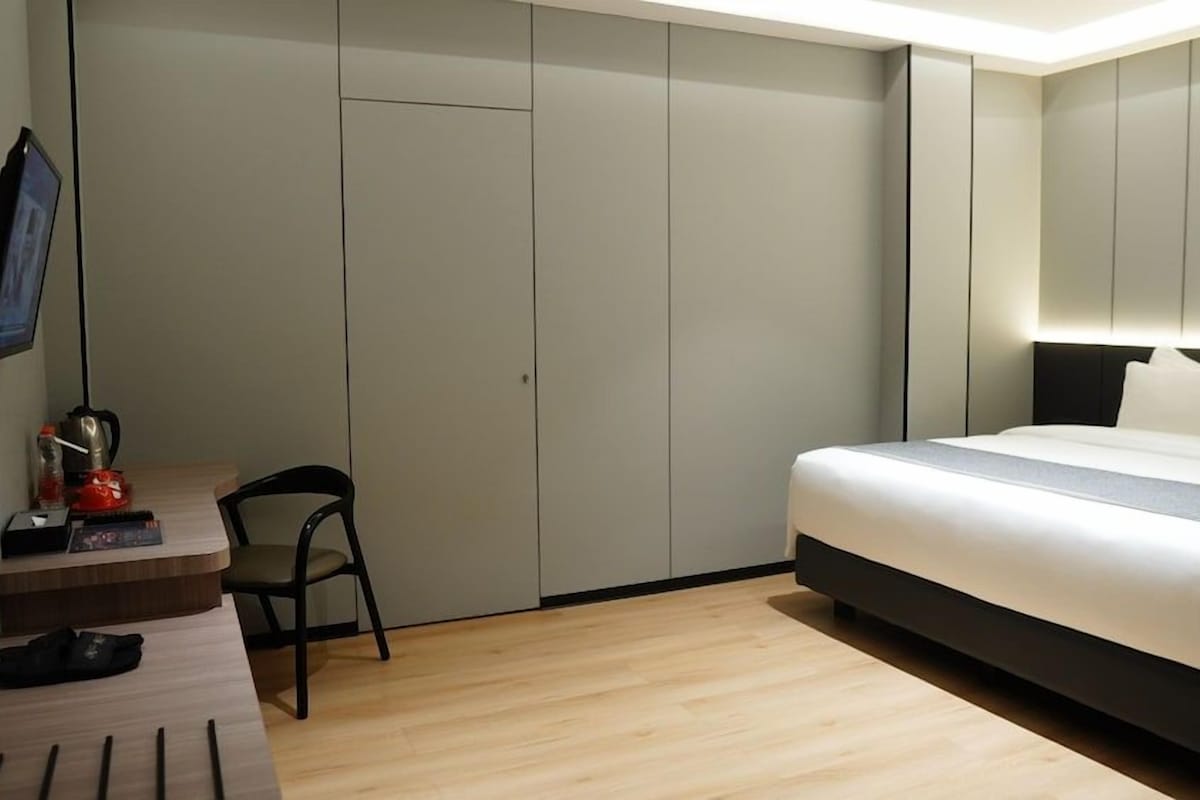 A hotel room with a bed, a desk with a chair, a TV, and a wardrobe.
