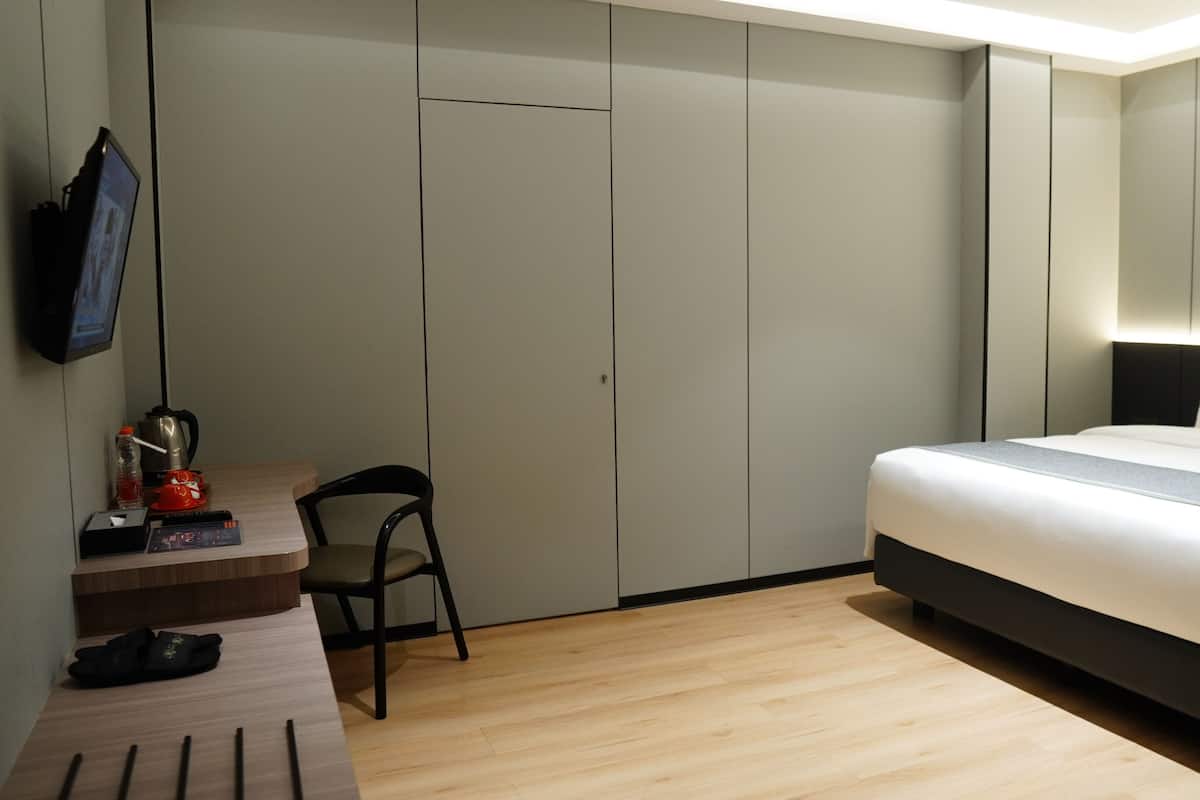 A hotel room with a bed, a desk with a chair, a TV, and a wardrobe.