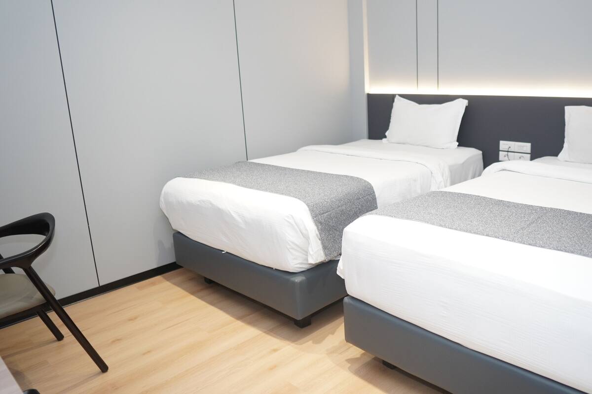 A hotel room with two beds, a chair, and a bedside table.