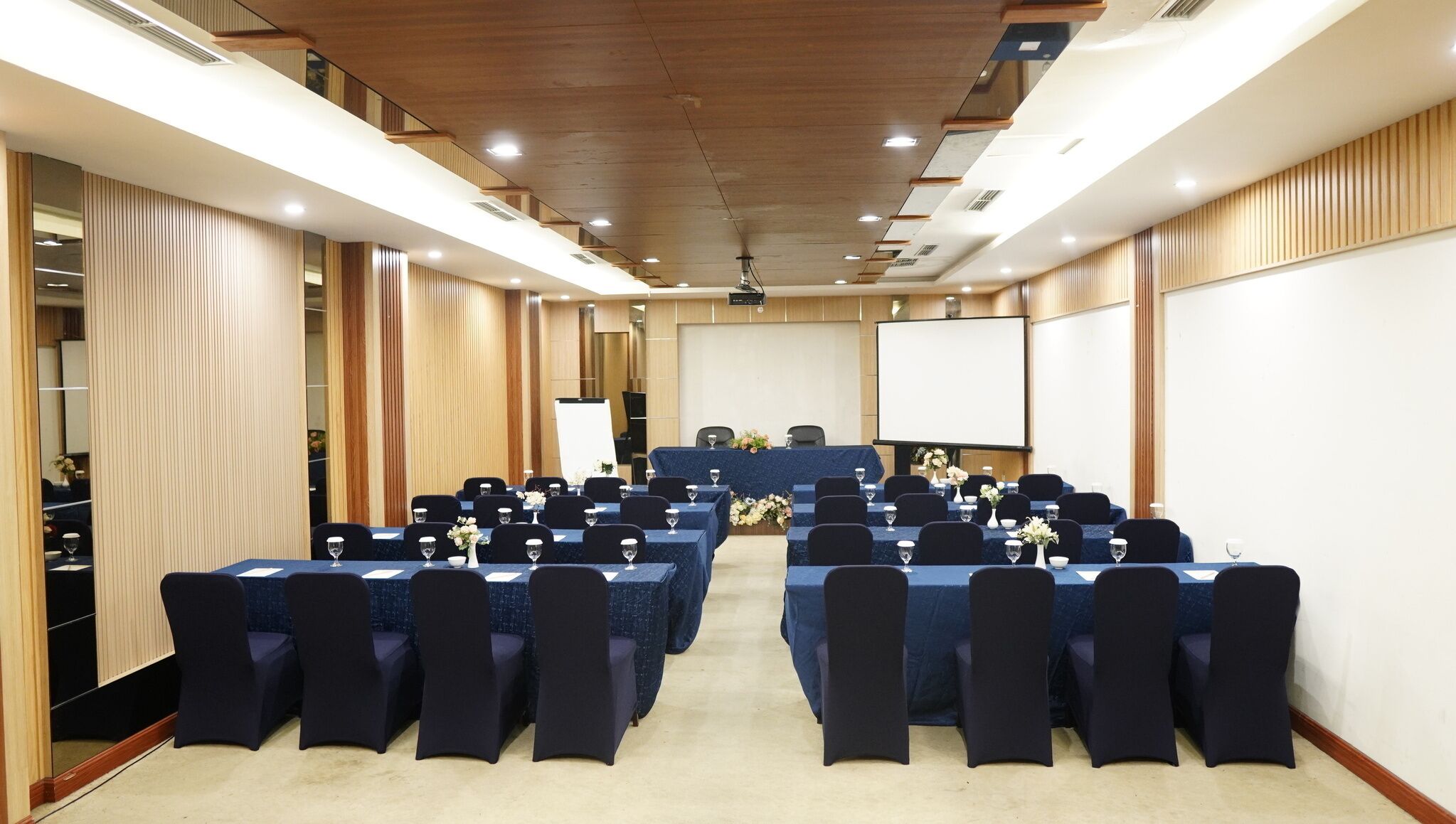 A conference room with rows of tables and chairs, a large screen, and a podium.