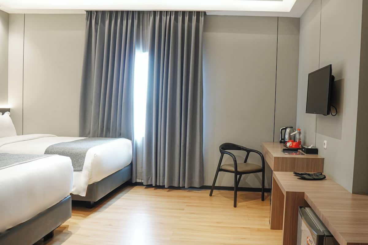 A hotel room with a bed, a desk, a chair, a television, and a window with curtains.