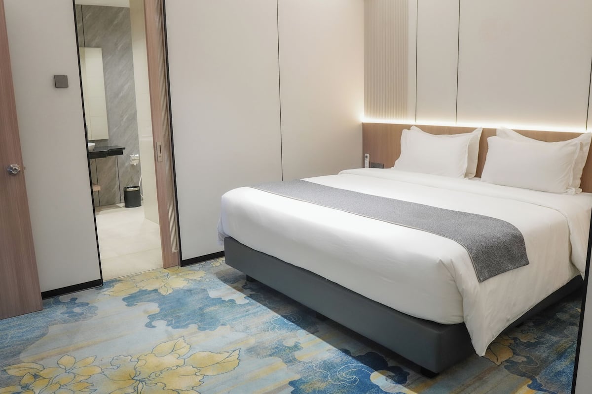 A hotel room with a bed, a bathroom visible through an open door, and a patterned carpet.
