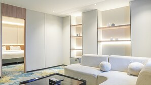 Een moderne hotelkamer met een bed, een slaapbank, een salontafel en inbouwplanken met verlichting.