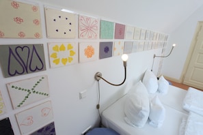 A hotel room with a neatly arranged wall of artwork, a bedside lamp, and a neatly made bed with pillows. - Hotel Artgenossen (Lindlar)