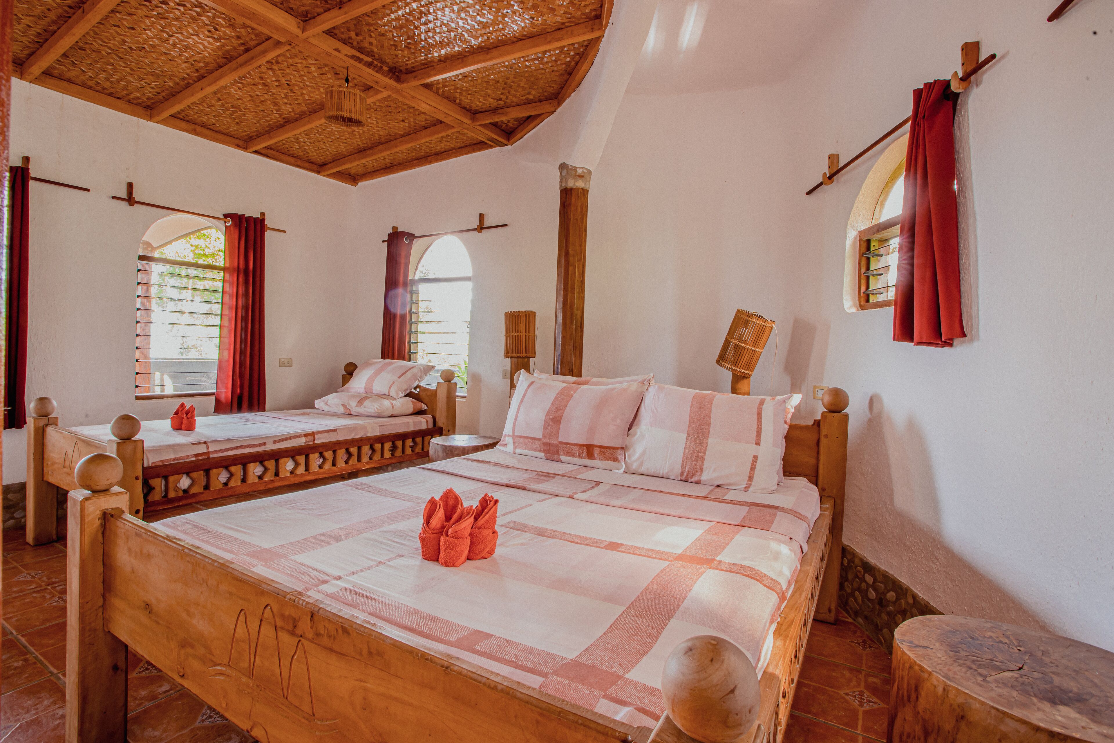 A traditional room with two wooden beds, a woven ceiling, and a stone wall.