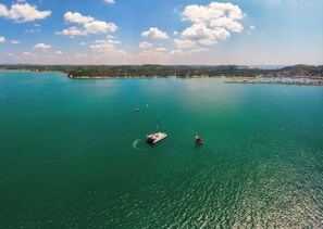 Vista aérea de una zona costera con una gran masa de agua, varios barcos y una costa distante con edificios y vegetación.