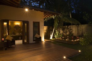 A wooden deck with a seating area, a small pool with lights, and a palm tree.