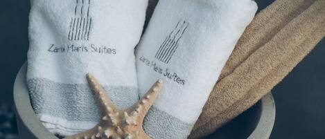 Dos toallas blancas con el bordado "Zane Maris Suites", ubicadas en un recipiente de piedra con una estrella de mar.