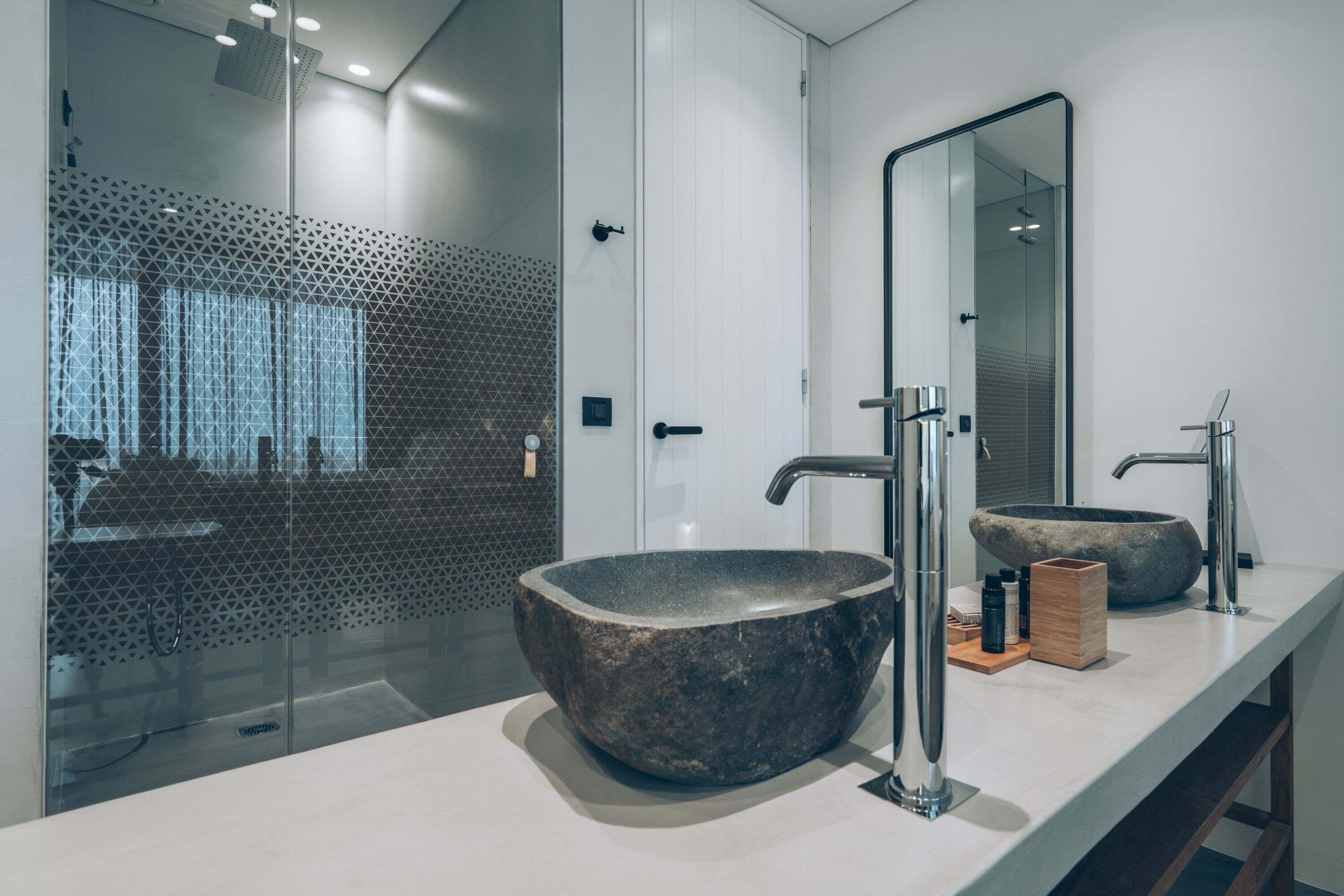 Un baño moderno con un lavabo de piedra grande, un espejo y una zona de ducha con puerta de vidrio geométrico.