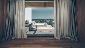 A room with a view of the sea, wooden flooring, a sofa, a table, and sheer curtains. - Zante Maris Suites - Adults Only (Zakynthos)